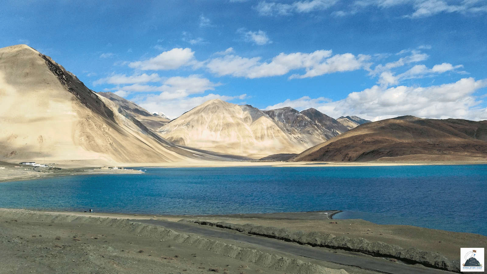 Turquoise Pangong Lake beneath bare brown mountains under a blue sky with white clouds