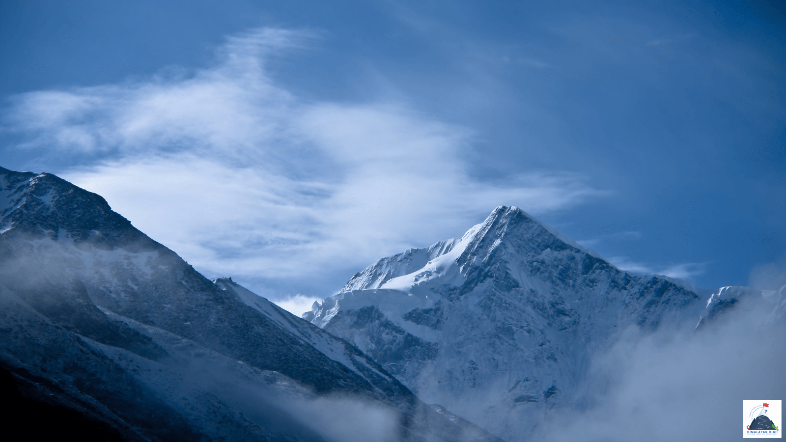 A sharp snow peak rising out of drifting cloud under a deep blue sky