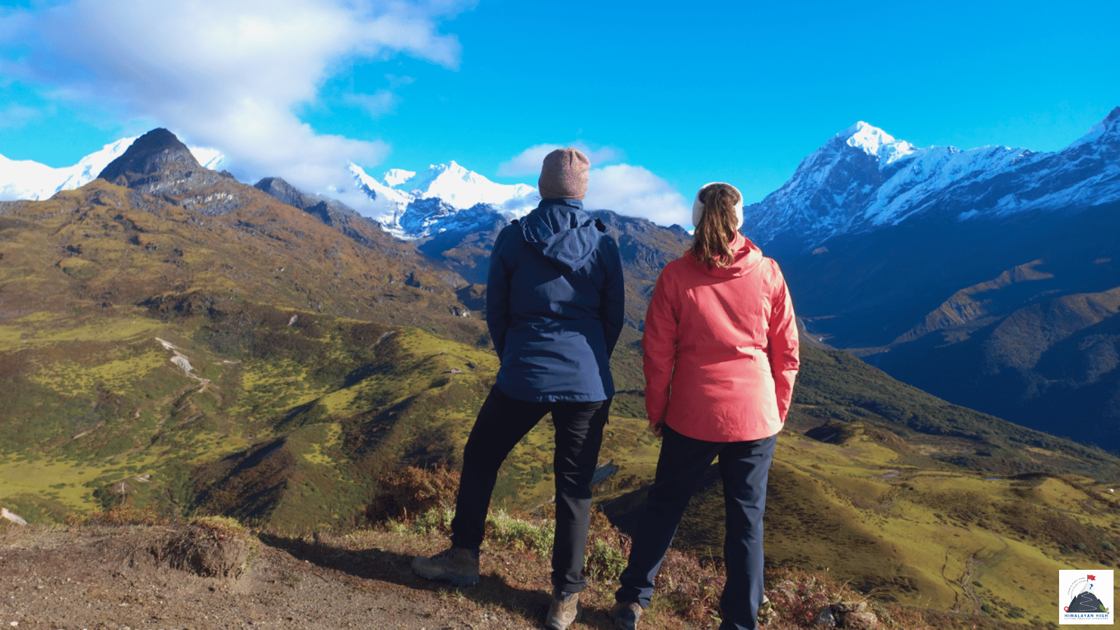Two trekkers looking out over green slopes to the snow peaks around Kanchenjunga