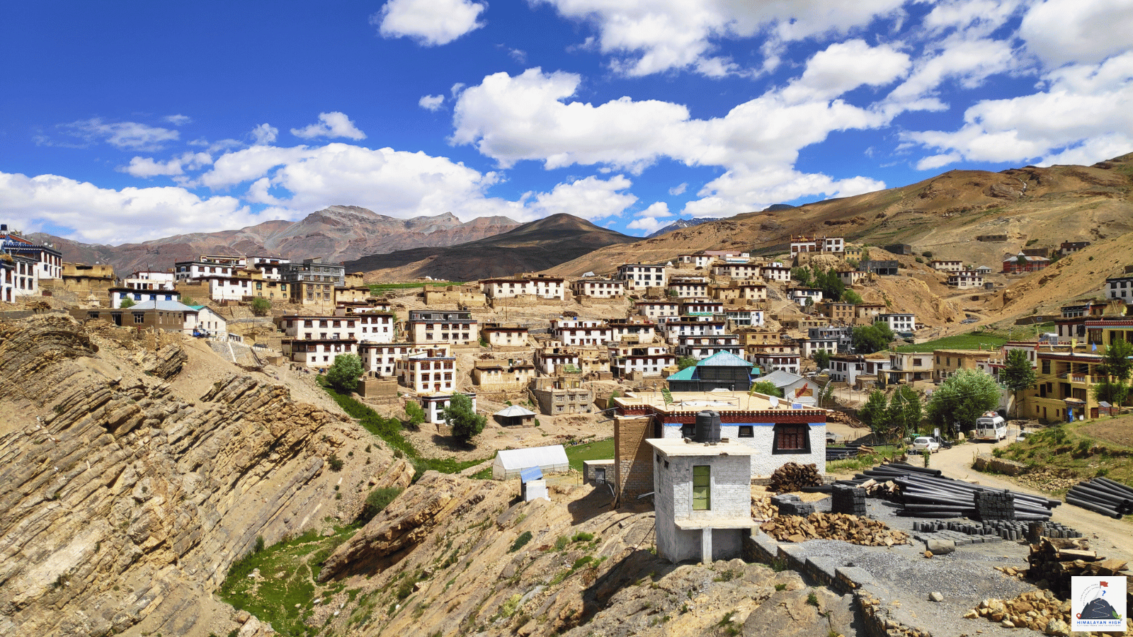 Whitewashed houses of Kibber village in Spiti stepped up a rocky slope under a blue, cloud-flecked sky